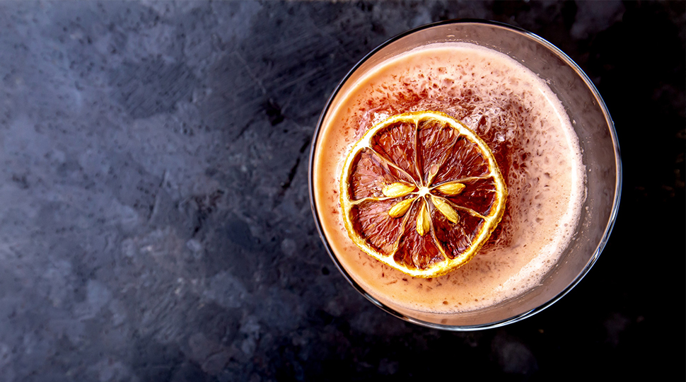 Orange-coloured cocktail with a dried orange garnish