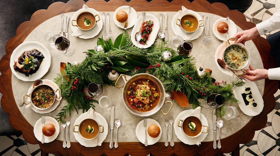 Overhead view of an oval table filled with holiday dishes with a large evergreen garland in the centre