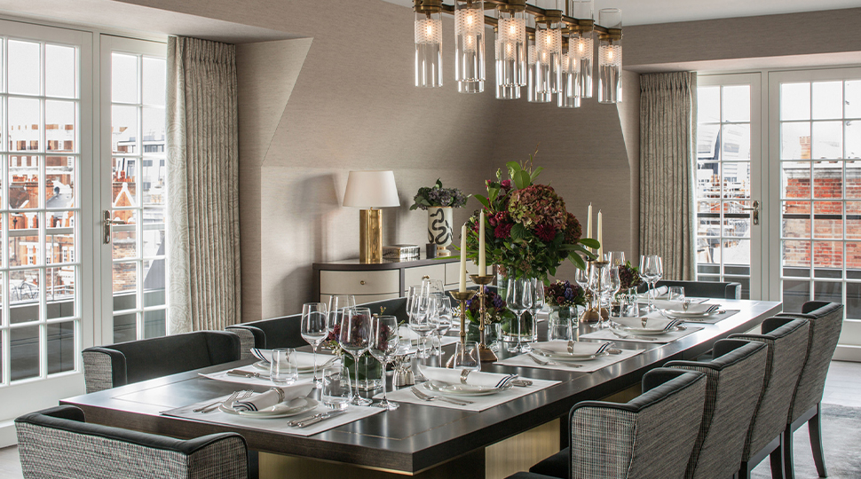 Dining room with long, black rectangular table set for 10, glass chandelier, credenza in the corner and white French doors on two walls