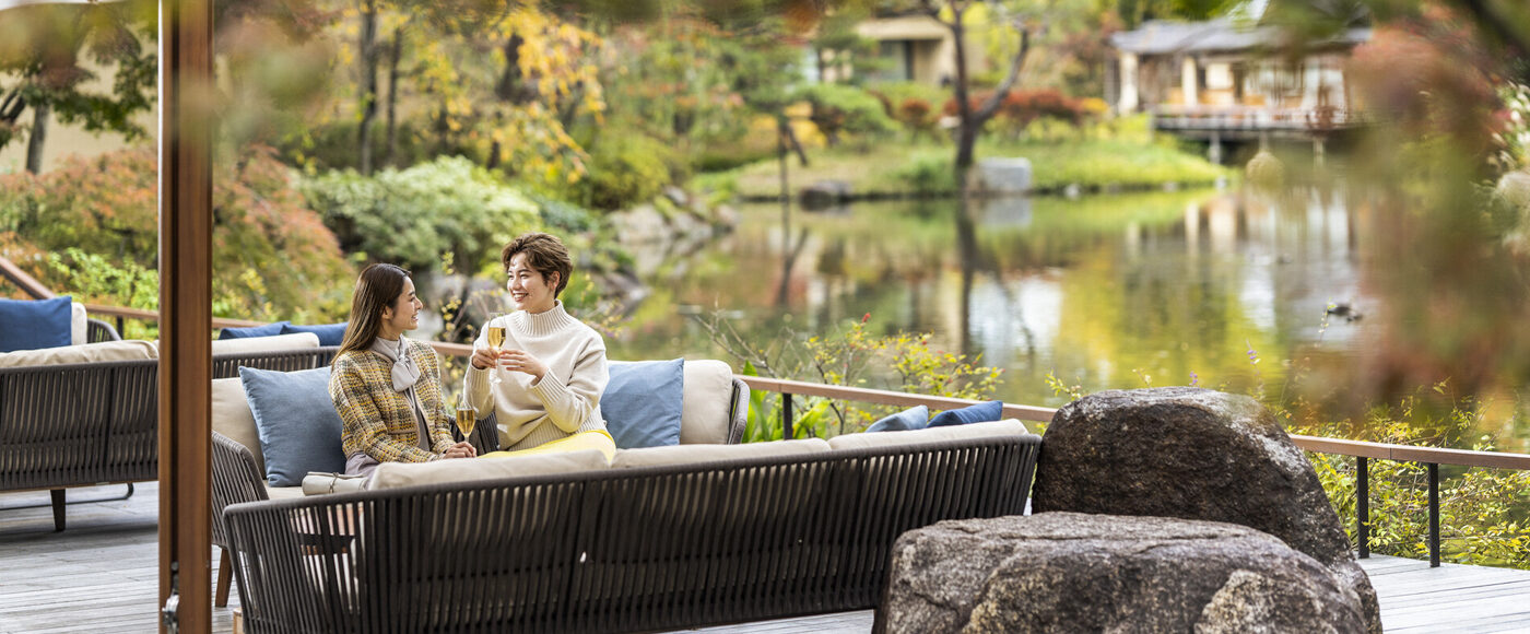 Two people sitting on an outdoor sofa, enjoying drinks by a tranquil pond garden at Four Seasons
