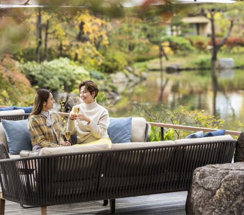 Two people sitting on an outdoor sofa, enjoying drinks by a tranquil pond garden at Four Seasons