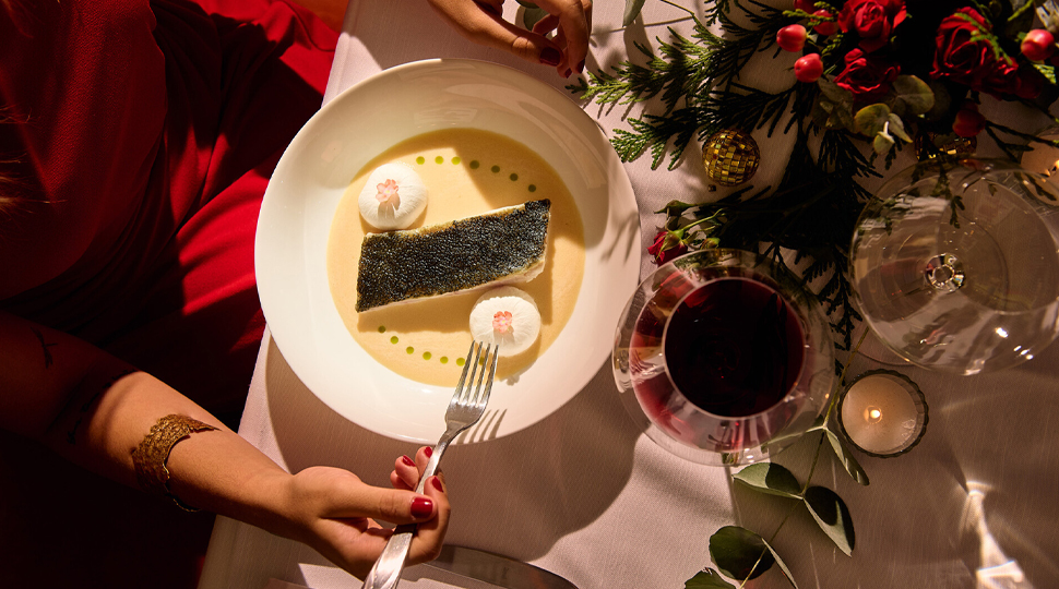 Round bowl of seafood set in front of a pair of hands on a table decorated with holiday decor